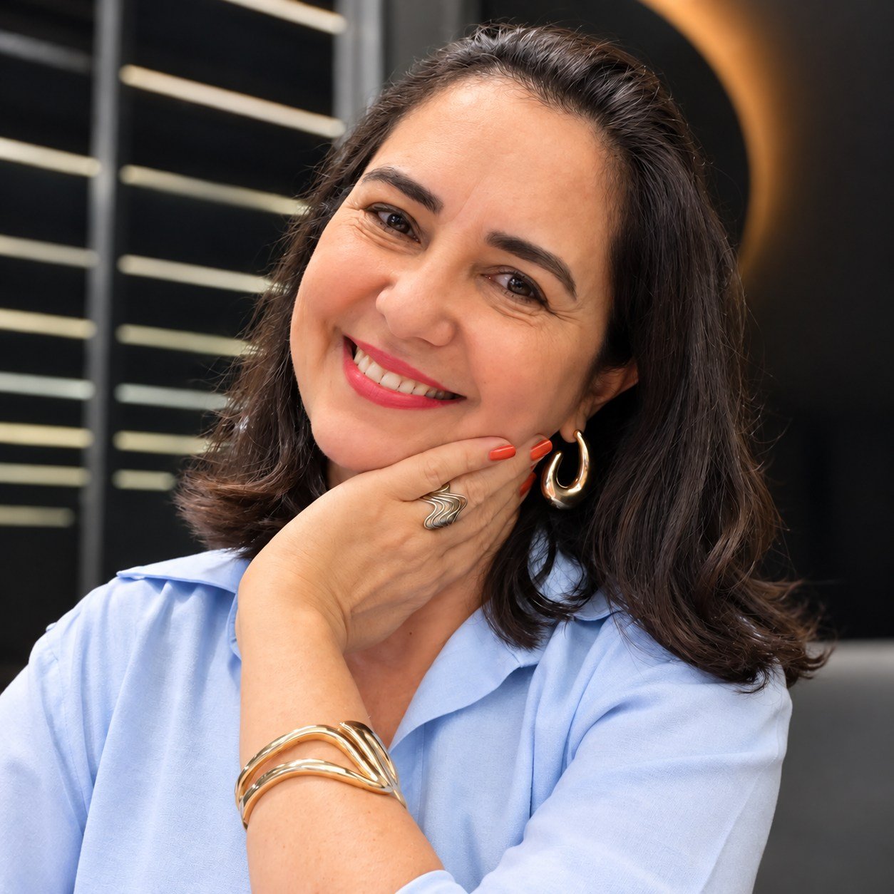 Micheli Romanezi sorrindo, de camisa azul clara, com a mão apoiada no rosto